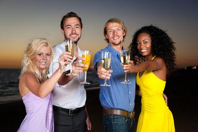 People (two couples) on the beach having a party, drinking and having a lot of fun in the sunset, they are wearing smart casual clothes and drink champagne