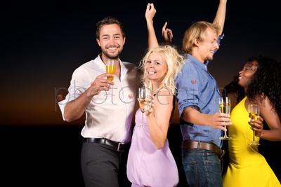 People (two couples) on the beach having a party, drinking and having a lot of fun in the sunset, they are wearing smart casual clothes and drink champagne