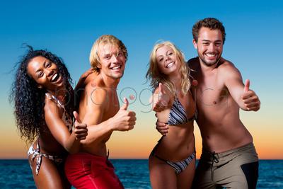 People (two couples) on the beach having a party, dancing and having a lot of fun in the sunset 
